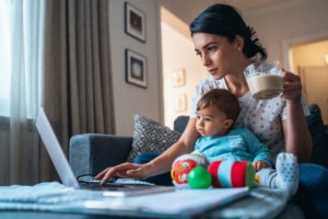 Caregiver with a baby using laptop at home.